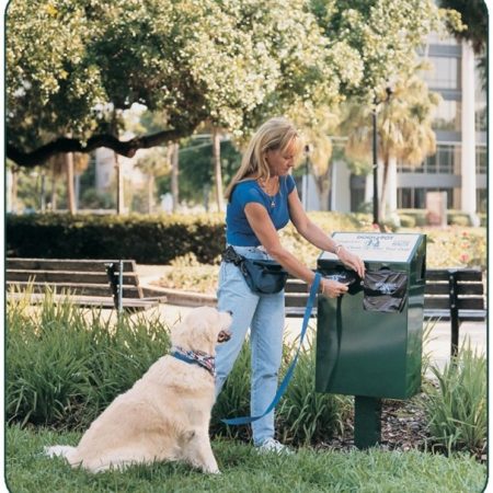 Woman disposing dog waste in green bin at park with golden retriever sitting nearby.