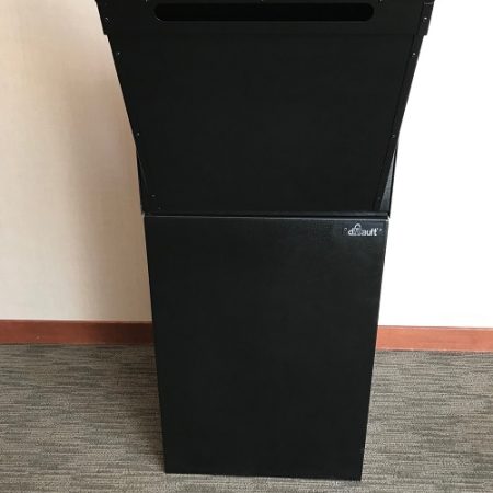Black podium with a slanted top and a logo on the front, placed on a carpeted floor against a wall.