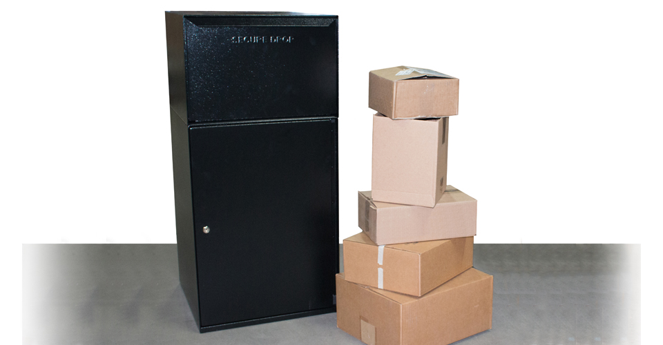 Black secure drop box next to a stack of cardboard packages on a gray surface.