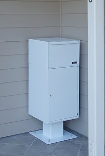 White parcel delivery box in a corner on a tiled floor against beige siding.
