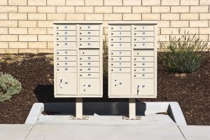 Two beige outdoor cluster mailboxes with numbered compartments against a brick wall.