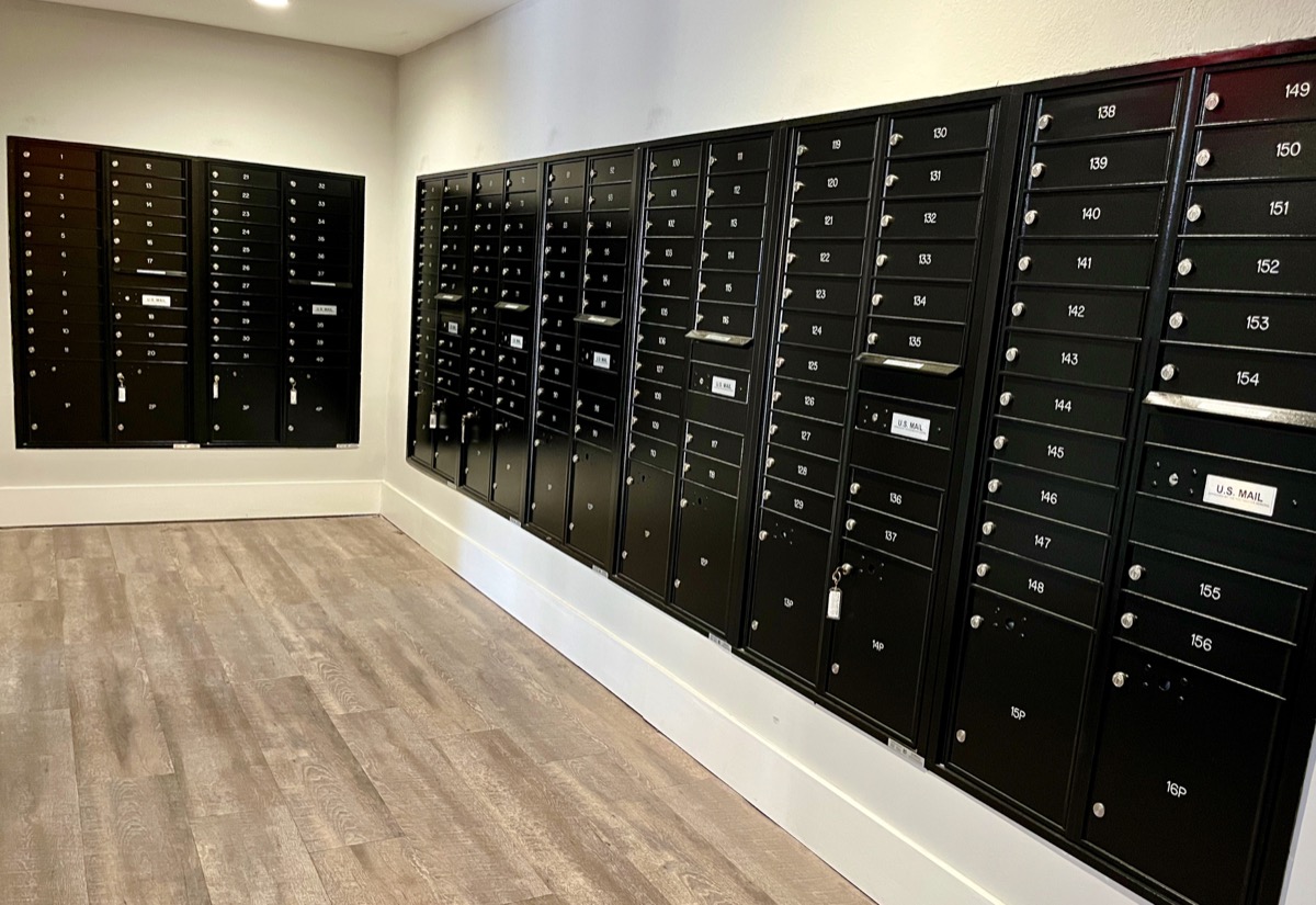 Black wall-mounted mailboxes with numbered compartments in a room with wood flooring.