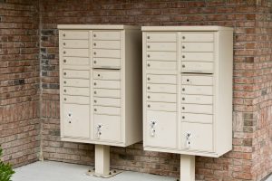 Two beige metal cluster mailboxes mounted against a brick wall.
