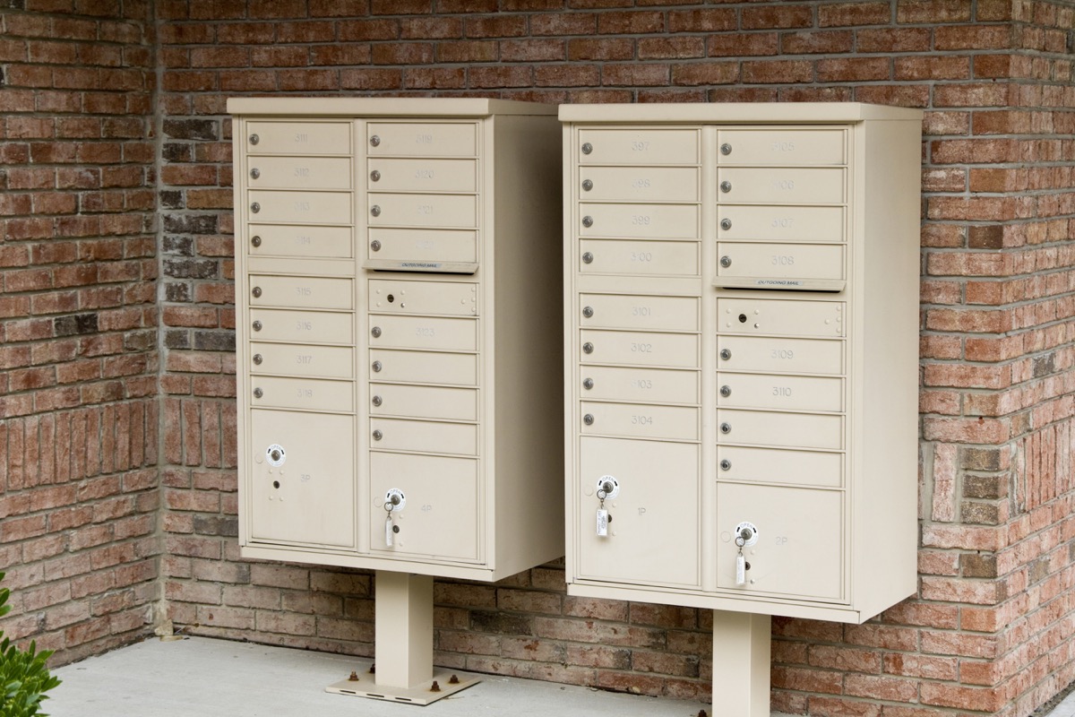 Two beige metal cluster mailboxes mounted against a brick wall.