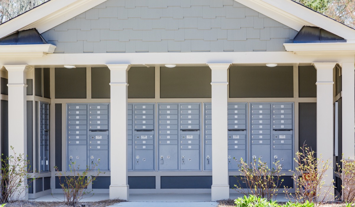 Outdoor community mailbox structure with multiple gray mailboxes and white pillars.