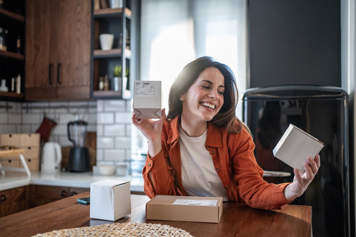 Woman in a kitchen smiling while holding small packages.