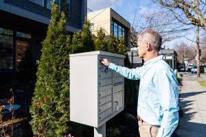 Man in blue shirt unlocking a community mailbox on a sunny residential street.