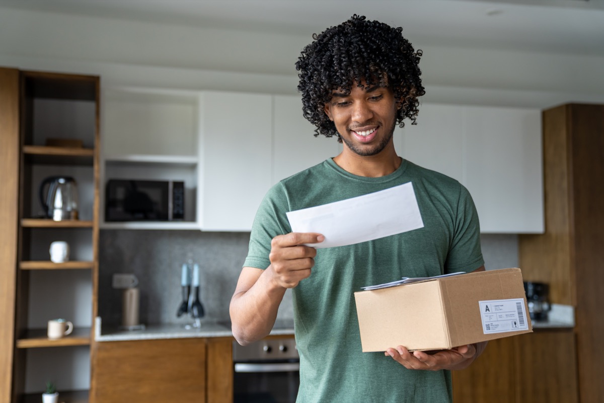 Person in a kitchen holding a cardboard package and reading a letter.