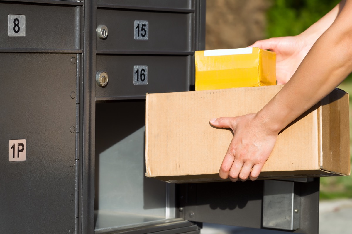 Hands placing packages into a metal mailbox with numbered compartments.