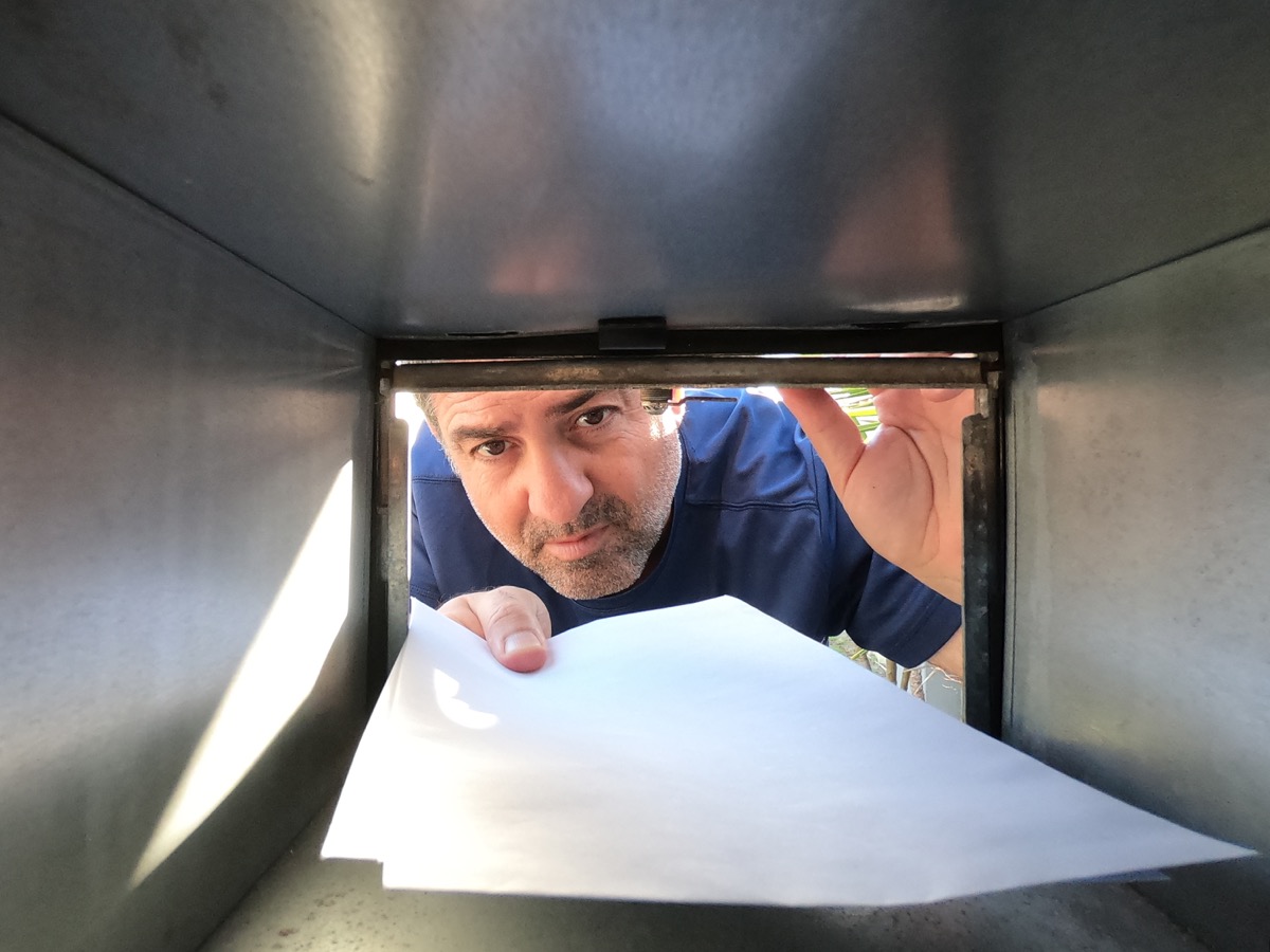 Man placing a white envelope into a metal mailbox, viewed from inside.
