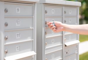Hand unlocking a gray outdoor mailbox with numbered compartments.
