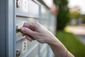 Hand inserting key into a metal mailbox lock outdoors.
