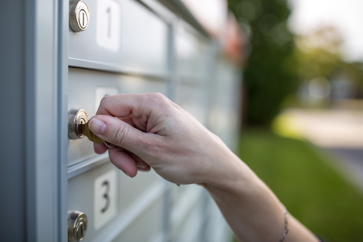 Hand inserting key into a metal mailbox lock outdoors.