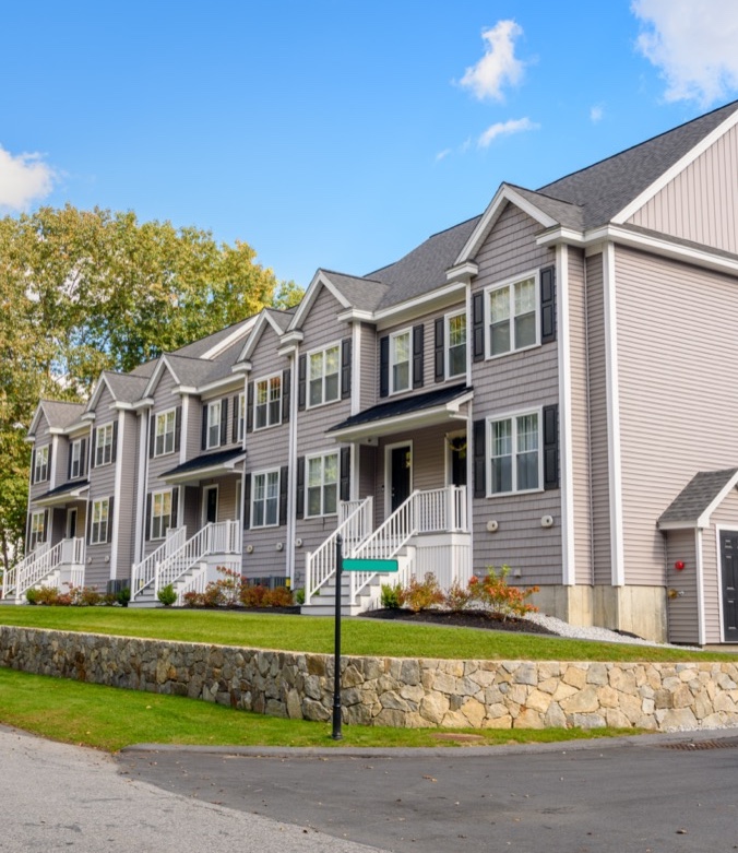 Row of modern townhouses with gray siding, white trim, and front porches, set against a clear blue sky.